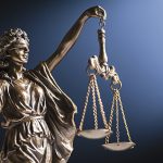 Bronze figurine of a blindfolded Lady Justice with her scales representing law and order on a blue background with copy space; Bronzefigur einer Lady Justice mit verbundenen Augen und ihrer Waage, die Recht und Ordnung auf blauem Hintergrund mit Kopierraum darstellt.