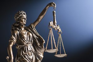 Bronze figurine of a blindfolded Lady Justice with her scales representing law and order on a blue background with copy space; Bronzefigur einer Lady Justice mit verbundenen Augen und ihrer Waage, die Recht und Ordnung auf blauem Hintergrund mit Kopierraum darstellt.